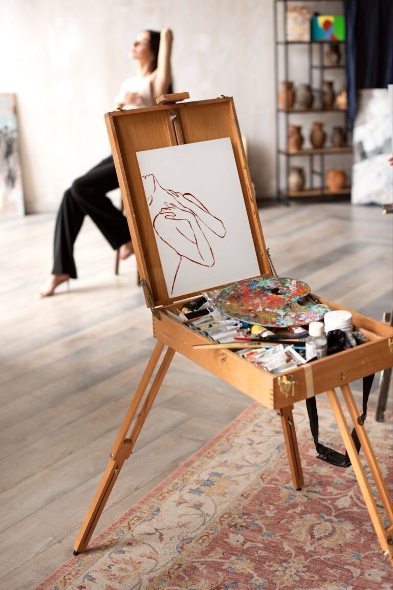 An open wooden sketch box with a palette, paints and a drawing